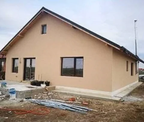 Casă în execuție, cu fațada tencuită și tâmplăria montată, pe șantier